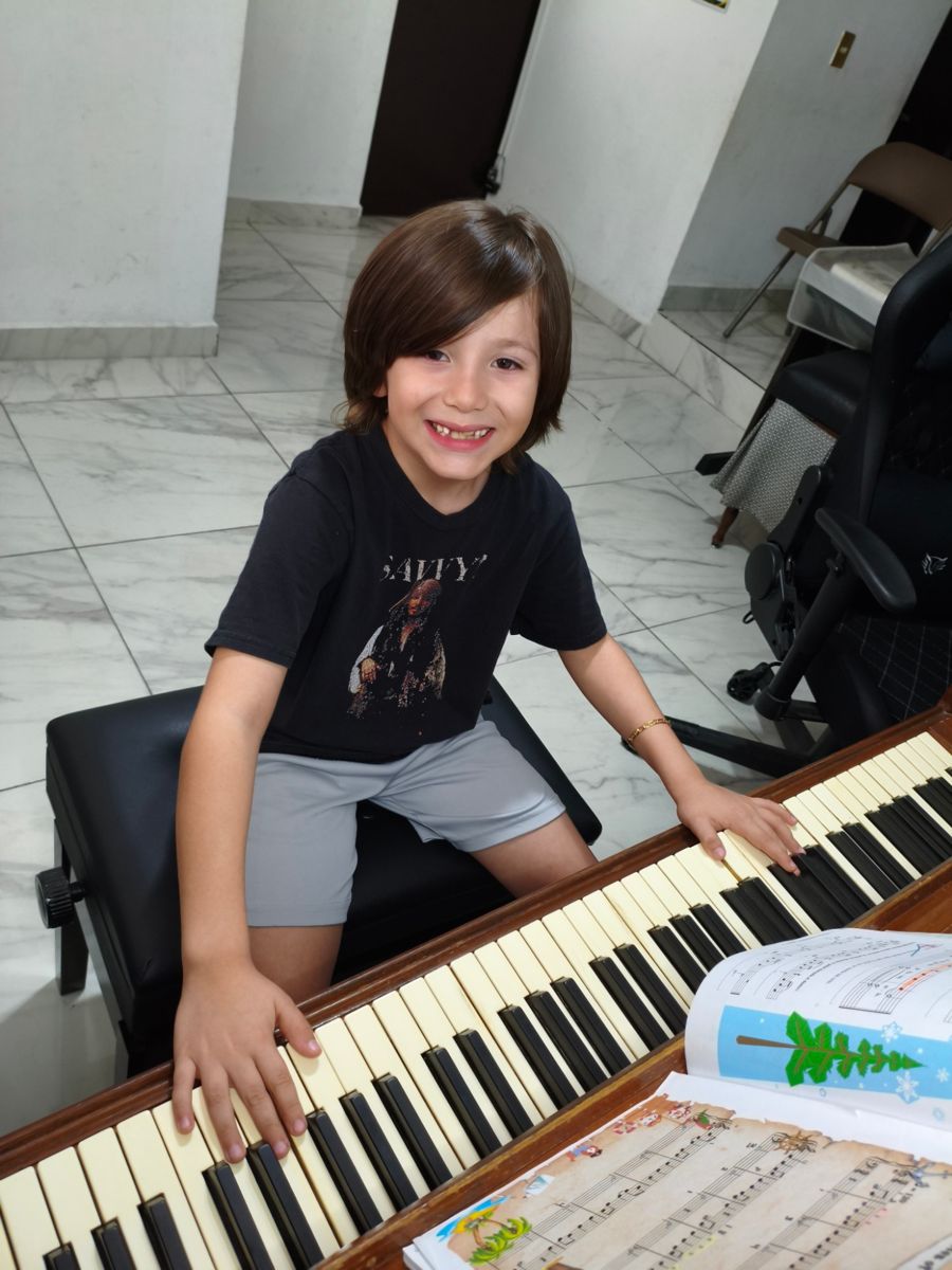 Un niño sonríe con las manos sobre el teclado del piano y un libro de música abierto